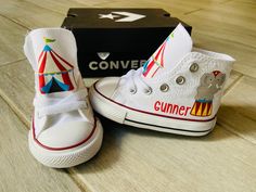 a pair of white sneakers with circus themed shoes on the bottom, and a box behind them