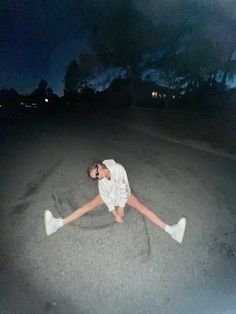 a person laying on the ground in the middle of an empty road at night time