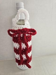 a red and white crocheted water bottle cover hanging from a hook on a wall