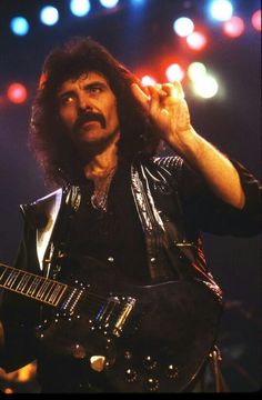 a man with long hair holding a guitar in his right hand and looking off to the side