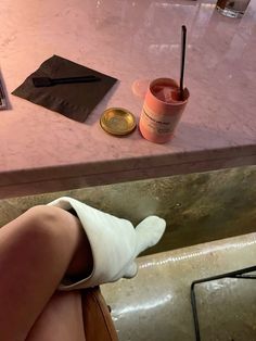 a woman sitting at a table with her legs up on the counter next to a cup