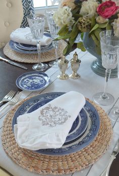 the table is set with blue and white plates, silverware, and flowers in vases