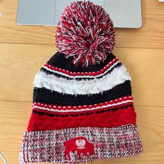 a red, white and black hat sitting on top of a wooden floor next to a laptop