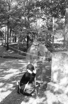 black and white photograph of a person kneeling in front of a grave with an umbrella