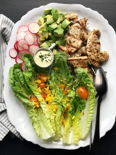 a white plate topped with lettuce and chicken next to sliced radishes