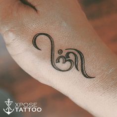 a small tattoo on the wrist of a person's left hand with an omen symbol