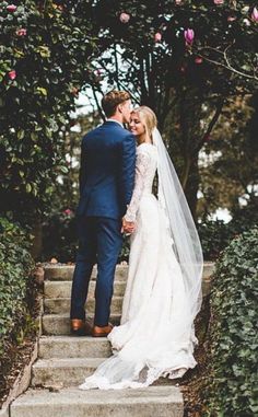 a bride and groom walking up some steps together in front of trees with pink flowers