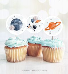 three cupcakes with blue frosting and planets on top are shown in front of a white background