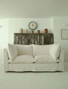 a living room with a white couch and clock on the wall