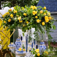 a table with yellow roses and blue vases on it, surrounded by greenery