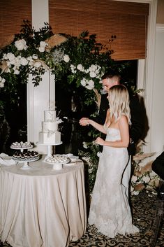 a man and woman standing next to each other in front of a table with a cake on it