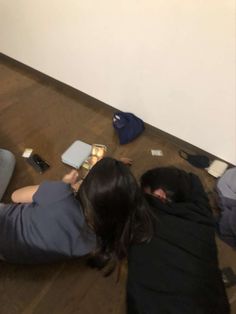 two people sitting on the floor looking at their cell phones while they are reading books