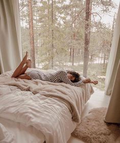 a woman laying on top of a bed in a bedroom next to a tree filled forest