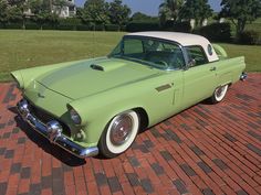 an old green and white car is parked on the brick walkway in front of a house