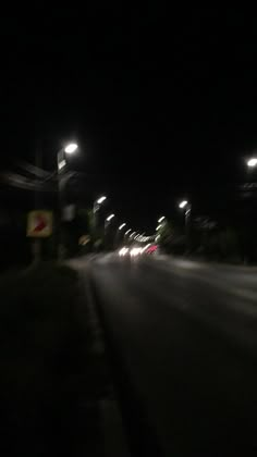 an empty street at night with lights on and cars driving down the road in the distance