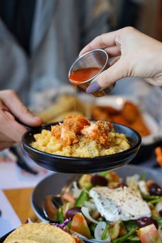 a person pouring sauce over a plate of food on top of a table with other plates