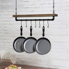 three pots and pans hanging from hooks on a white brick wall in a kitchen