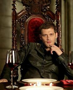 a man sitting in a chair next to a table with plates and wine glasses on it