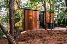 a small wooden cabin in the woods surrounded by trees and mulchy ground with lights on