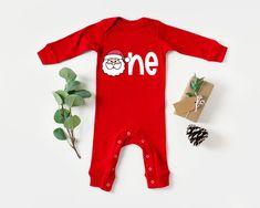 a baby's first christmas outfit, pine cones and presents on a white background