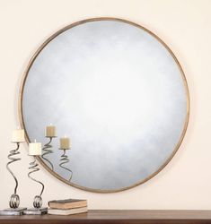 a round mirror sitting on top of a wooden table next to a lamp and two candles