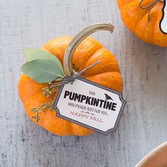 two pumpkins sitting next to each other on top of a wooden table with a tag