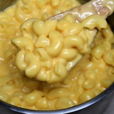 a spoon full of macaroni and cheese being stirred by a ladle in a pot