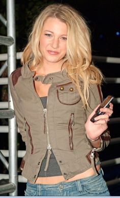 a woman is holding a cell phone and looking at the camera while standing in front of some stairs