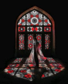 a person standing in front of a stained glass window with red and white designs on it