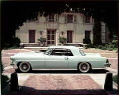 an old car is parked in front of a large building on a brick driveway area