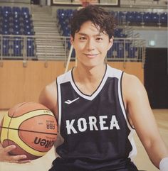 a young man holding a basketball sitting on top of a wooden floor in front of an arena