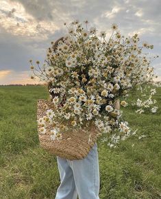 a woman carrying a basket full of daisies on her back in a grassy field