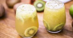 two glasses filled with liquid sitting on top of a table next to kiwis