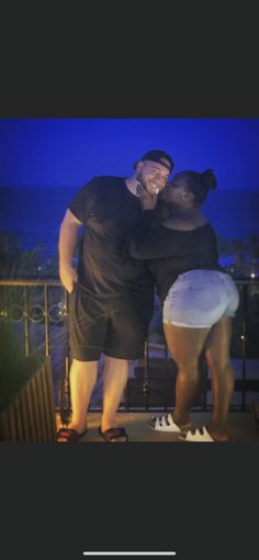 two people standing next to each other on a balcony with the ocean in the background