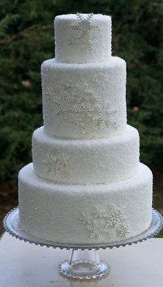 a three tiered white wedding cake sitting on top of a glass platter in front of trees