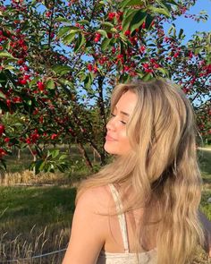 a woman standing in front of an apple tree with lots of red berries on it