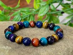 Elevate your style and enjoy the protective energies of Tiger's Eye with this stunning Multicolor Tiger's Eye Protection Bracelet. Handcrafted with care, this bracelet features high-quality 10mm Tiger's Eye beads in a captivating array of colors. The Multicolor Tiger's Eye beads showcase shades of blue, brown and purple. Please note that the blue, and purple colors on these beads are achieved through a color-enhancement process, highlighting the natural beauty of Tiger's Eye while adding an extr Square Tiger Eye Bead Bracelet, Tiger Eye Shaped Bead Bracelets, Meditation Bracelet, Unboxing Experience, Brown Bracelet, Yoga Bracelet, Tiger Eye Beads, Protection Bracelet, Eye Beads