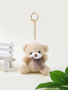 a teddy bear keychain sitting next to a small white bench and green plant