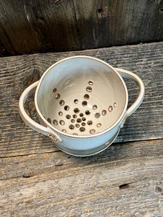 a blue bowl with holes in it sitting on a wooden table next to a wall