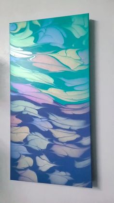 a painting hanging on the wall in a room with white walls and blue, green, pink, yellow and purple colors