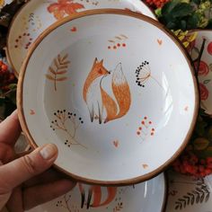 two bowls with foxes painted on them are being held by a person's hand