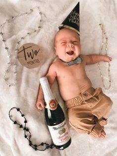 a baby wearing a party hat laying next to a bottle of champagne and a necklace