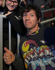 a man and woman standing next to each other in front of a metal railing with people behind them