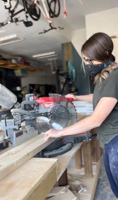 a woman in a mask working on a table saw