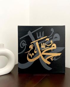 an arabic calligraphy is displayed on a table next to a coffee mug and vase