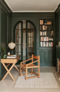 a living room with green walls and wooden chairs in front of a book shelf filled with books