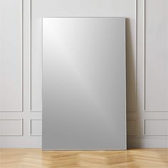 an empty mirror on the floor in front of a white wall and wooden flooring