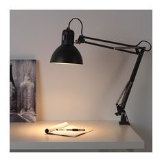 a desk lamp sitting on top of a white table next to a book and pen