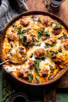 a casserole dish with meatballs, cheese and herbs in it on a wooden table