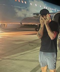 a man standing in front of an airplane on the tarmac talking on his cell phone